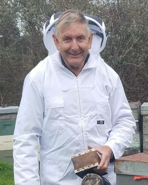 Lindsay Feary, Master Beekeeper, im weissen Imkeranzug mit Smoker vor seinen Bienenstöcken